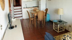 Un ambiente compatto con angolo cottura, zona pranzo e un piccolo tavolino con lampada.