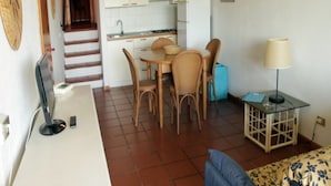 Un ambiente compatto con angolo cottura, zona pranzo e un piccolo tavolino con lampada.