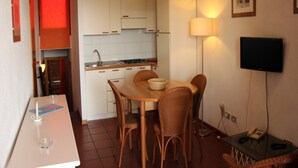 A compact kitchen with white cabinets, a dining table with wicker chairs, a small island, and a flat-screen TV mounted on the wall. - Apartment in Cannigione di Arzachena, Sardinia (Cannigione di Arzachena)