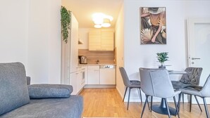 A modern living room with a grey sofa, a dining area with grey chairs, and a kitchen in the background. - Nice 1BR 1LR Apartment City Center (Vienna)