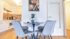 A modern kitchen with white cabinets, a dining table with two grey upholstered chairs, and a potted plant. - Nice 1BR 1LR Apartment City Center (Vienna)