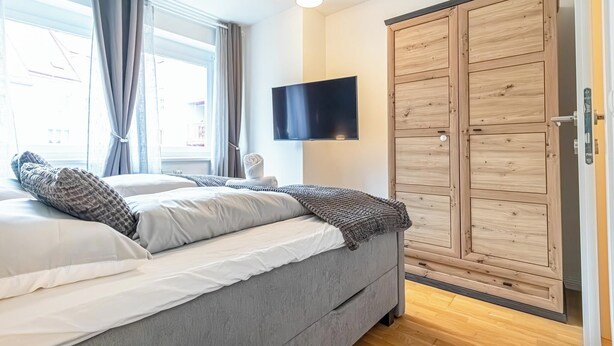 A bedroom with a bed, a TV mounted on the wall, and a wooden wardrobe. - Nice 1BR 1LR Apartment City Center (Vienna)