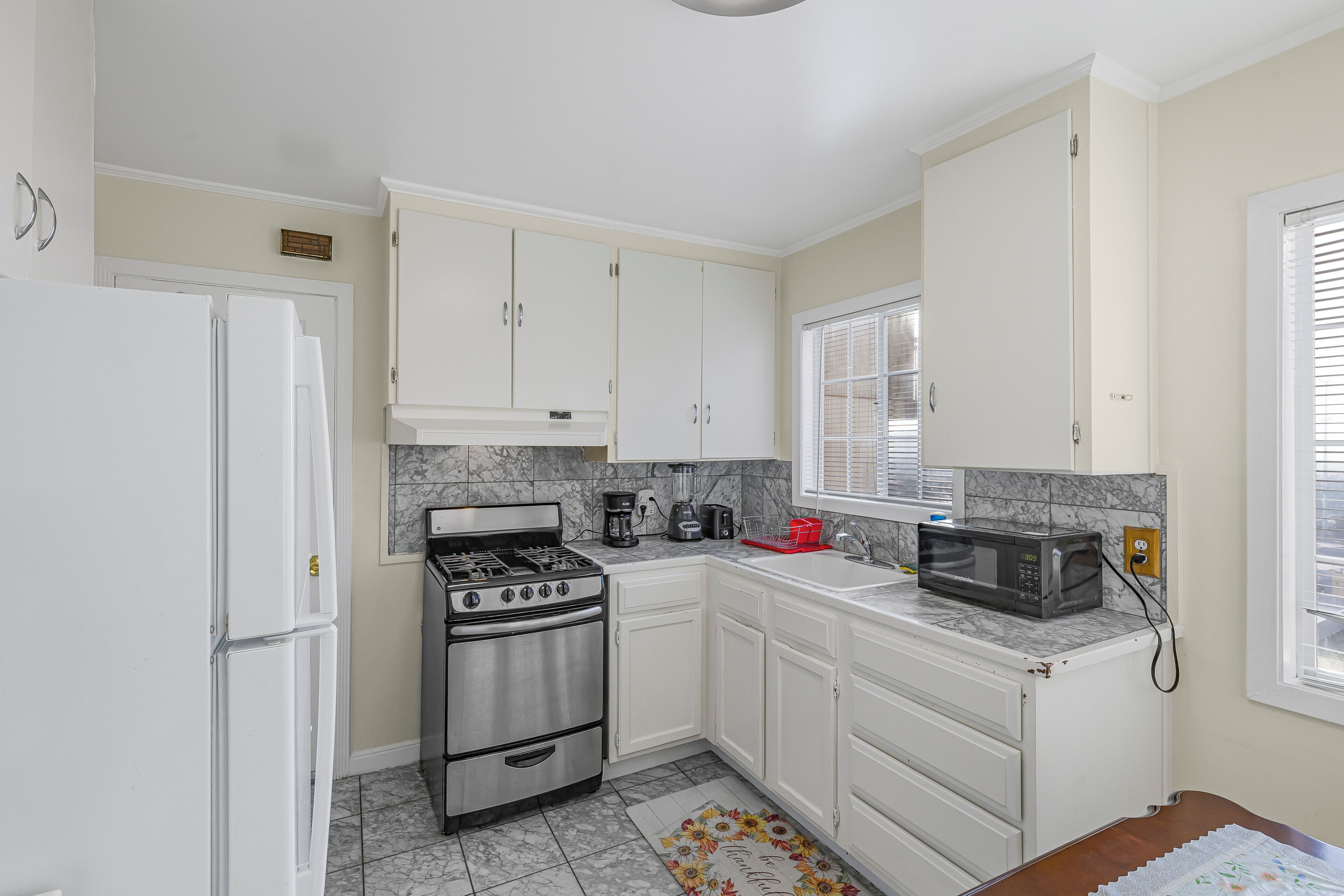 Una cocina con gabinetes blancos, estufa, microondas y refrigerador.