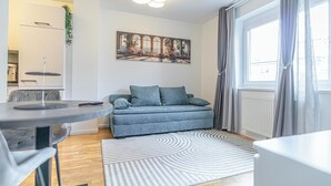 Una sala de estar moderna con un sofá gris, una mesa de comedor redonda y un amplio ventanal con cortinas.