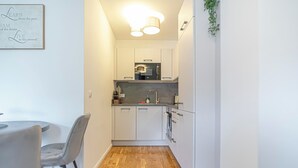 Una cocina compacta con armarios blancos, un comedor con mesa y sillas, y piso de madera.