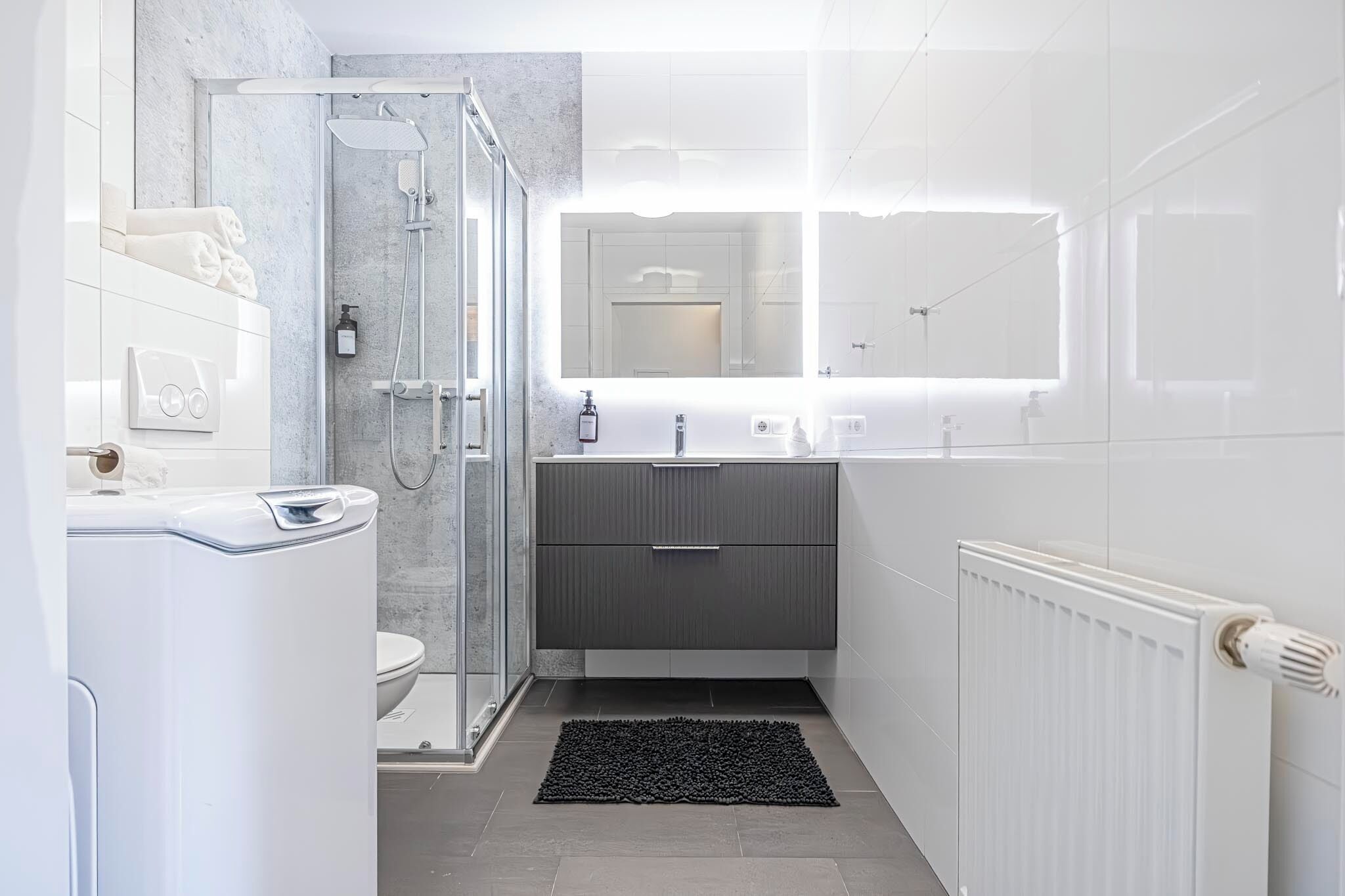A modern bathroom with a glass shower enclosure, a white toilet, a sink with a mirror, and a radiator.