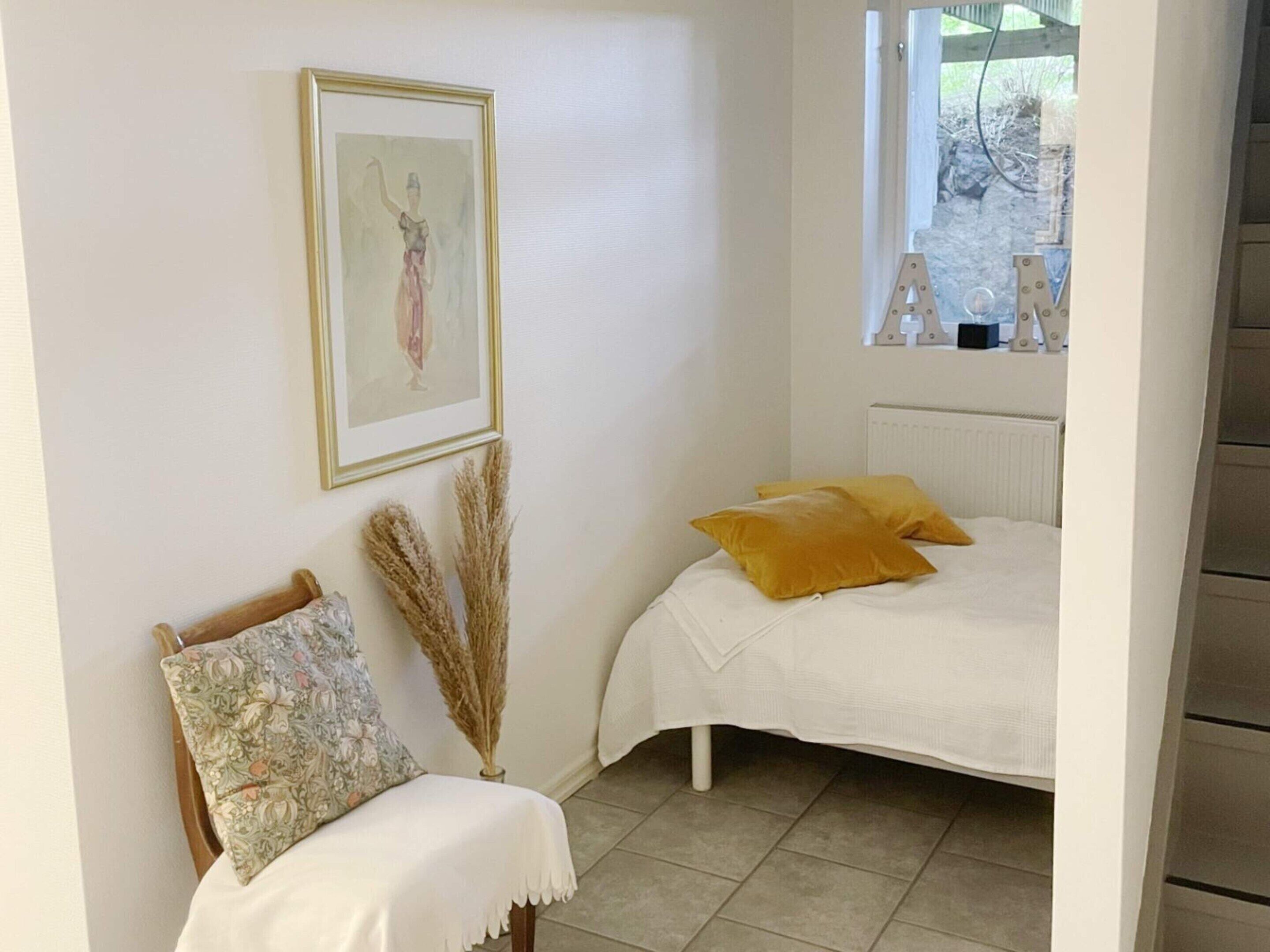 Ein Schlafzimmer mit einem Bett, einem Sessel, einem gerahmten Bild und einem Fenster.