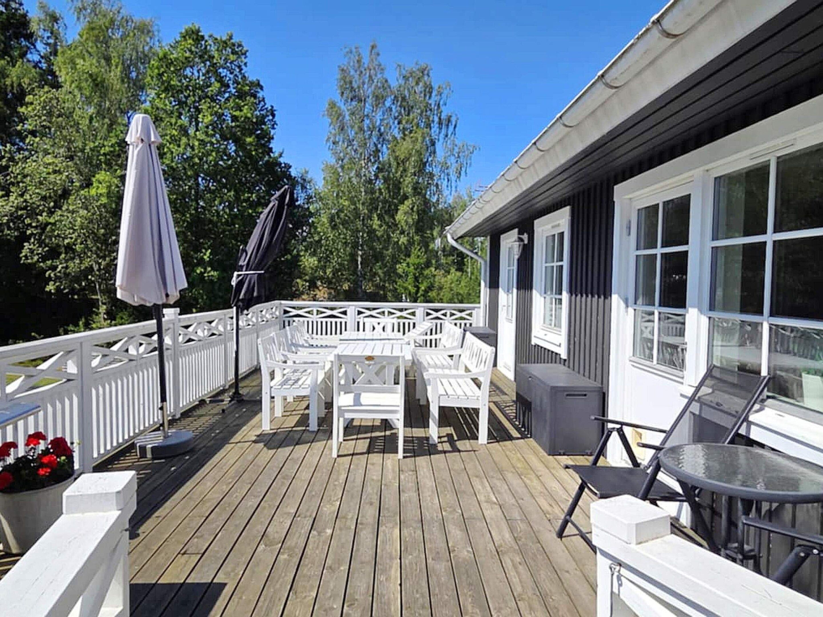 A wooden deck with white outdoor furniture, including tables and chairs, and a glass table on the right.