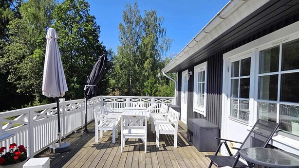 A wooden deck with white outdoor furniture, including a table and chairs, and a glass table on the right. - 5 Star Holiday Home in Vaxholm (Vaxholm)
