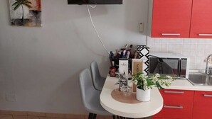 Eine moderne Küche mit Wand-Fernseher, roten Schränken, einer weißen Arbeitsplatte und einem Essbereich mit Stuhl und Tisch.
