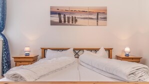 Una cama doble con ropa blanca, dos mesitas de noche con lámparas y un cuadro de atardecer en la pared.