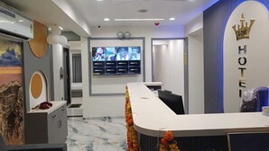 A hotel reception area with a curved reception desk, a large screen displaying multiple monitors, and a wall with a crown logo and the word "HOTEL". - hotel A-one (Gandhinagar)