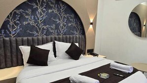A modern bedroom with a round bed, a decorative headboard, a ceiling fan, and an air conditioning unit. - hotel A-one (Gandhinagar)