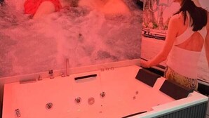 A spa area with a large hot tub, a sink, and a small stool. - hotel A-one (Gandhinagar)