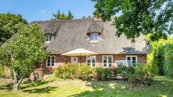 A house with a thatched roof, brick walls, and a small garden with flowering plants.