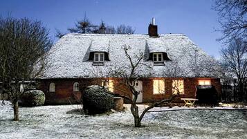 Una casa ricoperta di neve, con facciata in mattoni, tetto di paglia e un camino ben visibile.