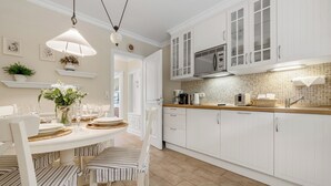 A kitchen with white cabinets, a microwave, and a dining area with striped chairs and a table set for four. - Cozy 3-room vacation apartment on approx. 80 m² for 4 persons. (Wenningstedt-Braderup (Sylt))