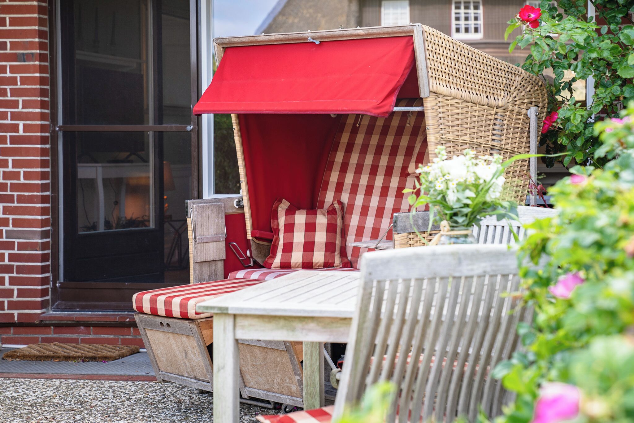 A wicker outdoor seating area with red and white checkered cushions, a wooden table, and a red awning.
