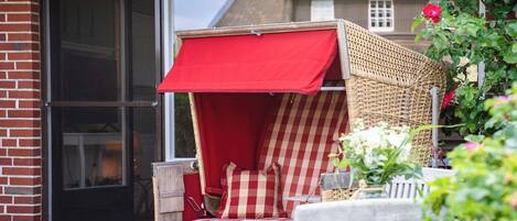 A wicker outdoor seating area with red and white checkered cushions, a wooden table, and a red awning.