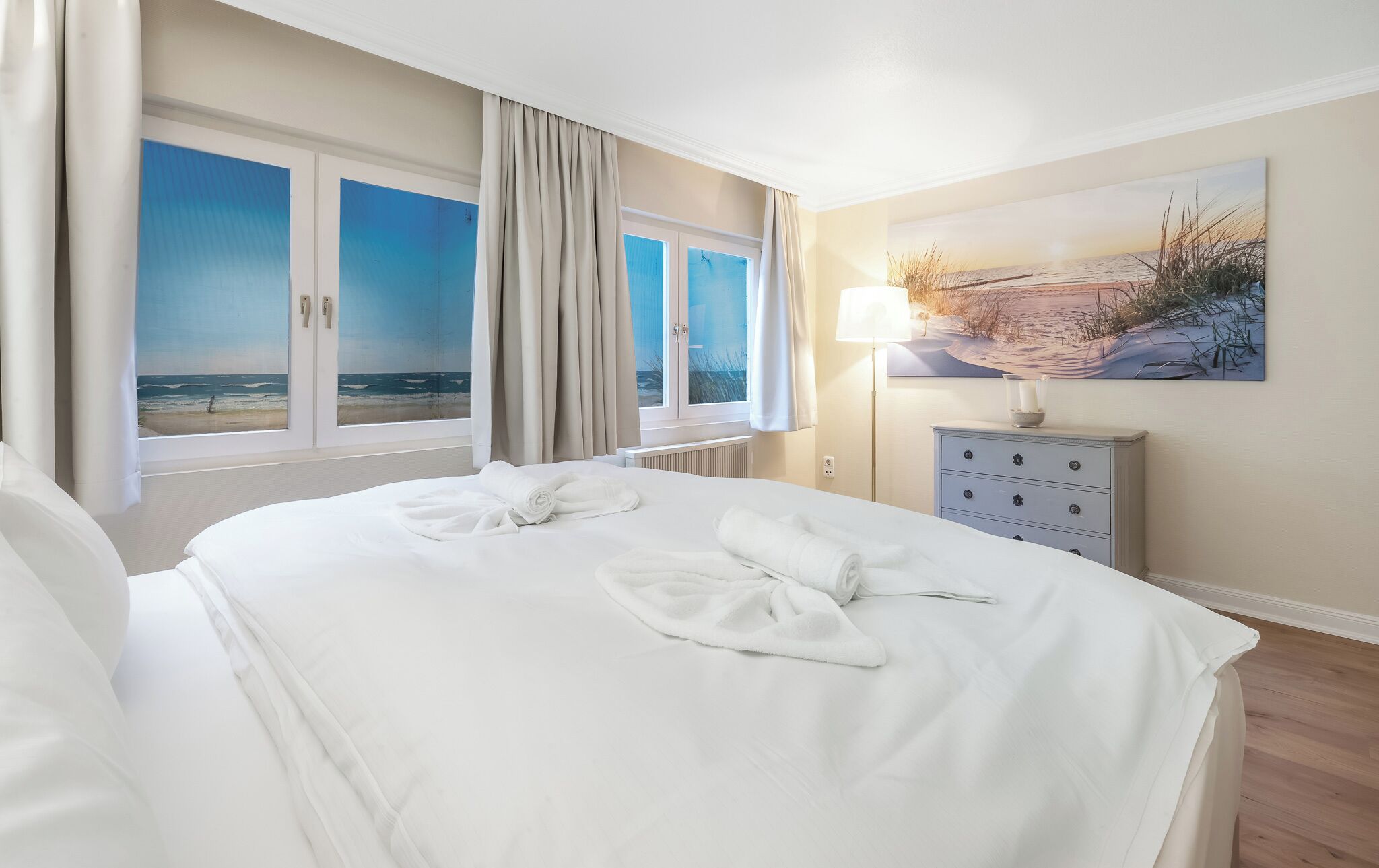 A hotel room with a bed, a nightstand, a lamp, and a painting of a beach scene.