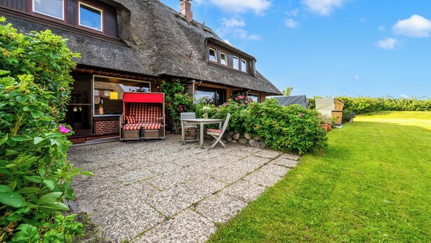 A house with a thatched roof, a gravel patio, and a lawn. - Cozy 3-room vacation apartment on approx. 80 m² for 4 persons. (Wenningstedt-Braderup (Sylt))