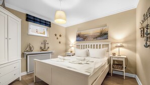 A bedroom with a bed, bedside tables, a dresser, a radiator, and wall decorations. - Cozy 3-room vacation apartment on approx. 80 m² for 4 persons. (Wenningstedt-Braderup (Sylt))