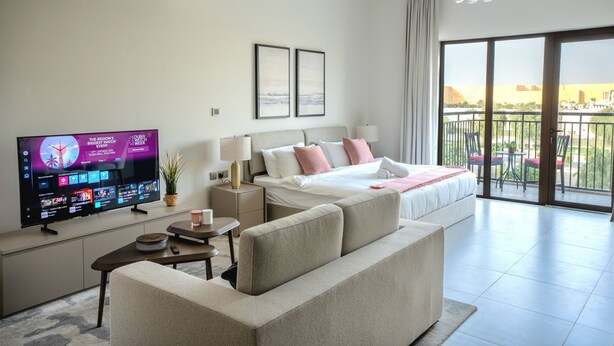 Een moderne hotelkamer met een groot flatscreen televisietoestel, een comfortabele bank, een netjes opgemaakt bed en een balkon met uitzicht.