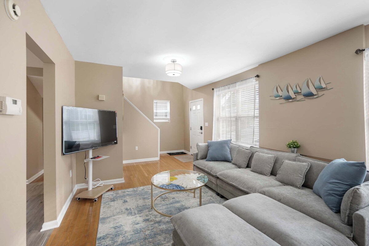 A living room with a grey sofa, a flat-screen TV, a coffee table, and a staircase leading to another room.
