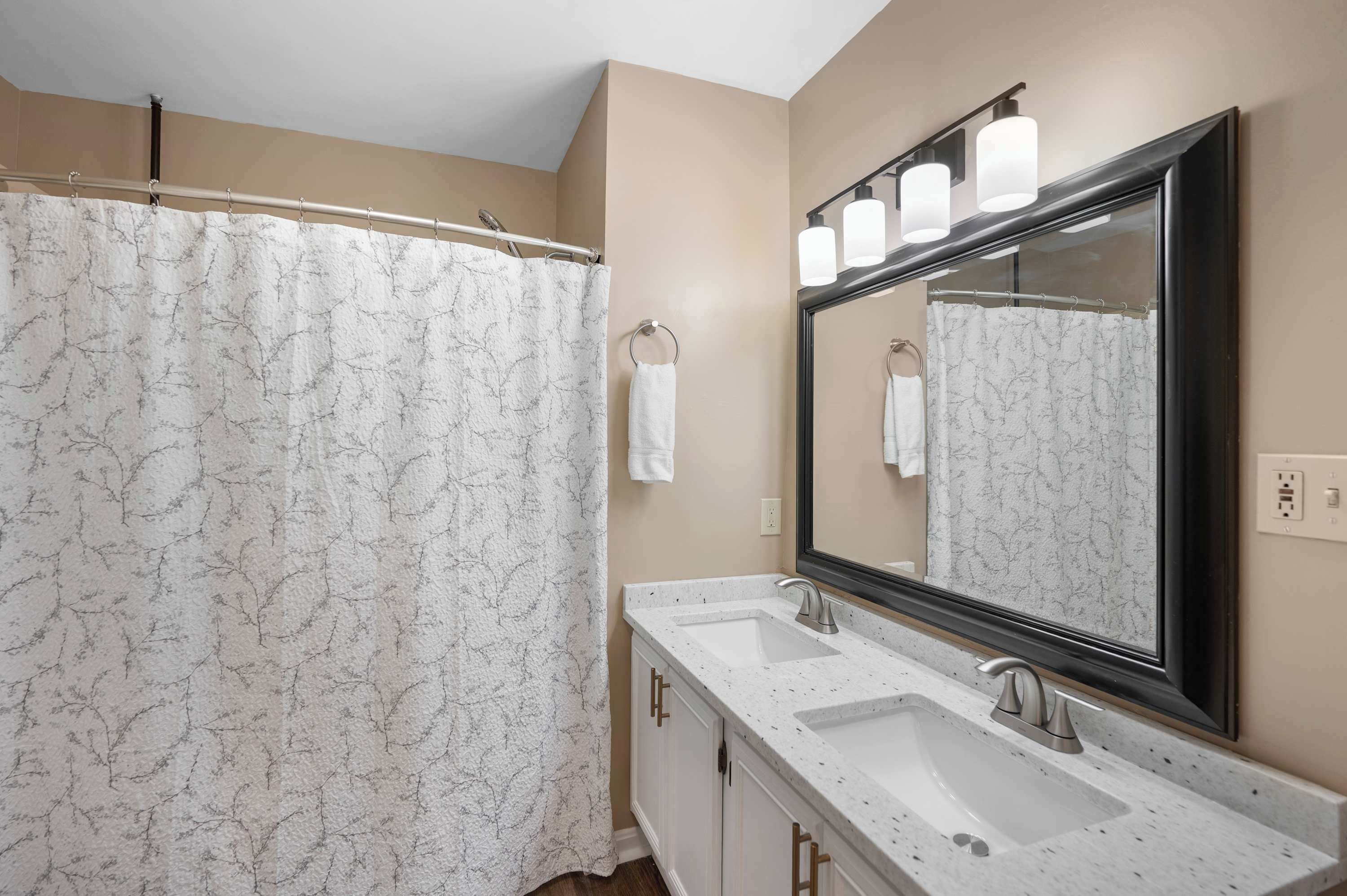 A bathroom with a shower curtain, a sink with a mirror, and a towel hanging on the wall.