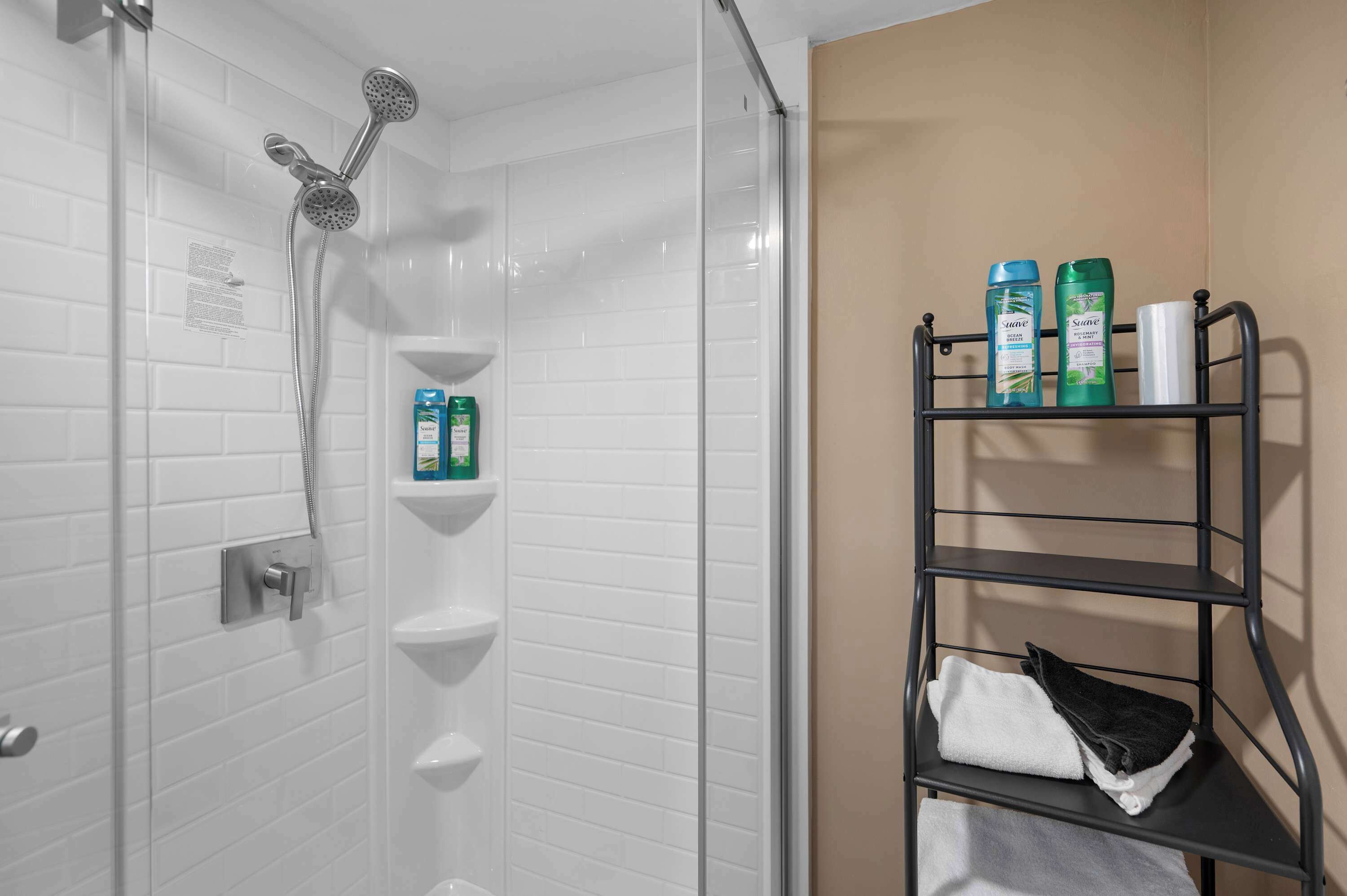 Ein Badezimmer mit Dusche, weißen Fliesenwänden, einem Ablagefach für Pflegeprodukte und einem Handtuchhalter.