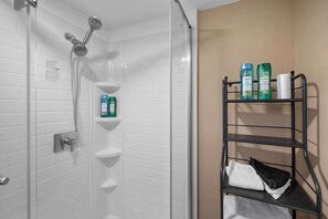 A bathroom with a shower, white tiled walls, a shelf with toiletries, and a towel rack. - Tusculum Hilltop Haven  For 8 (Cincinnati)