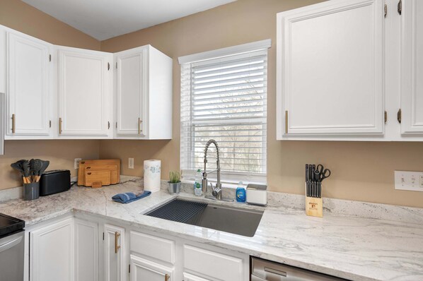 A kitchen with white cabinets, a black sink, and a window with blinds. - Tusculum Hilltop Haven For 8 (Cincinnati)