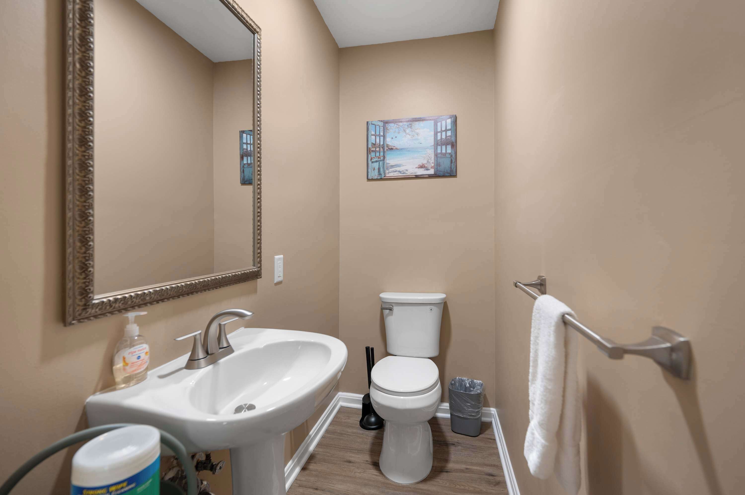 Une salle de bain avec un lavabo, des toilettes et un tableau représentant une scène de plage.