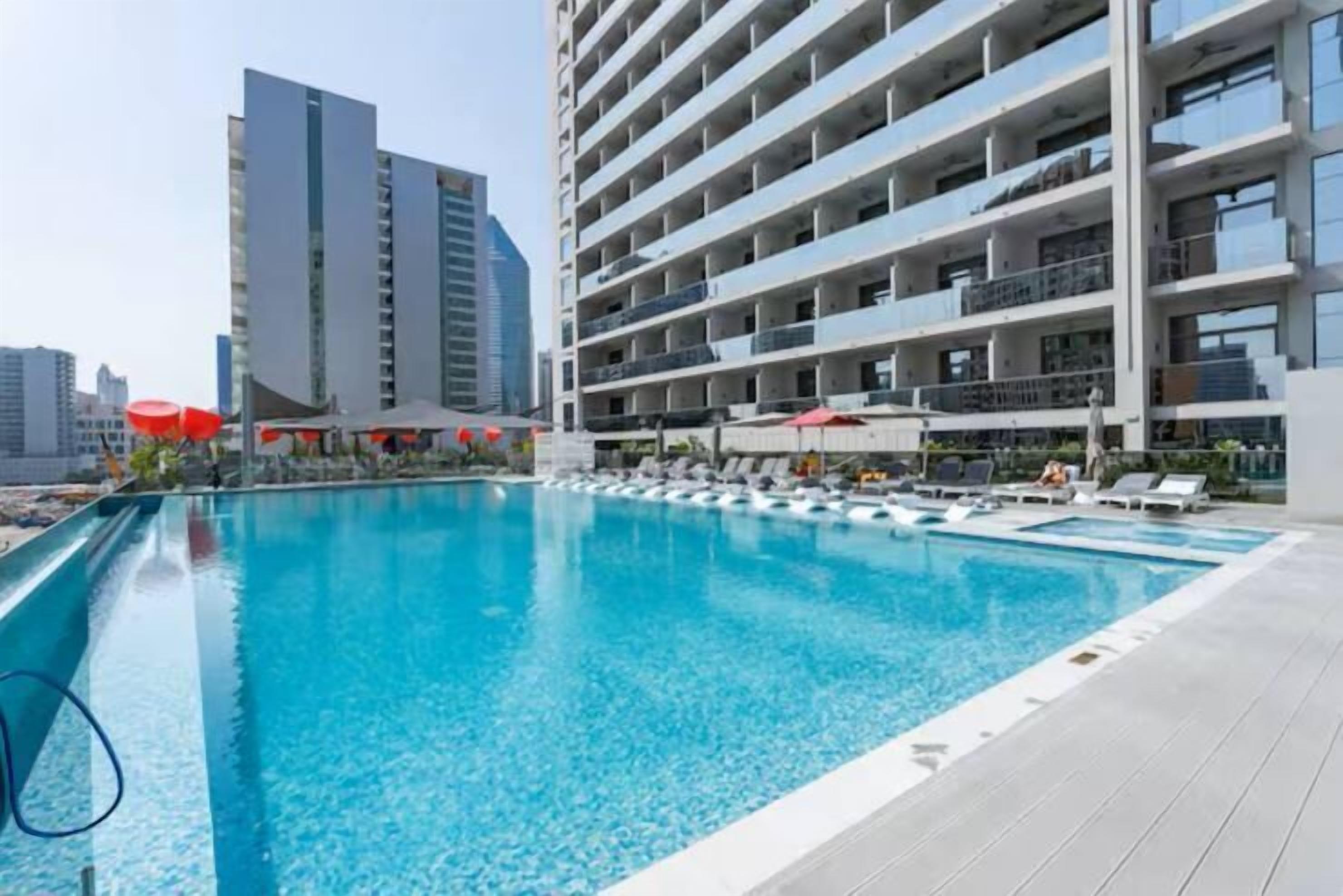 Un hotel moderno con una grande piscina, diversi balconi e vista su edifici circostanti.