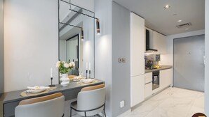 A modern kitchen with a built-in oven and microwave, a dining area with a table set for two, and a large mirror above the table. - Vogue| Downtown close to Burj Khalifa | Dubai Mall (Dubai)
