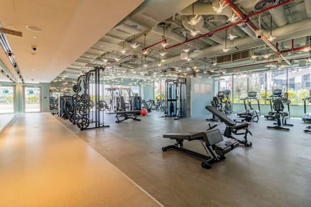Ein geräumiger Fitnessraum mit unterschiedlichen Trainingsgeräten, großen Fenstern und hoher Decke.