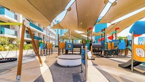 A playground with various play structures, including swings and climbing frames, set against a backdrop of modern buildings. - Vogue| Downtown close to Burj Khalifa | Dubai Mall (Dubai)
