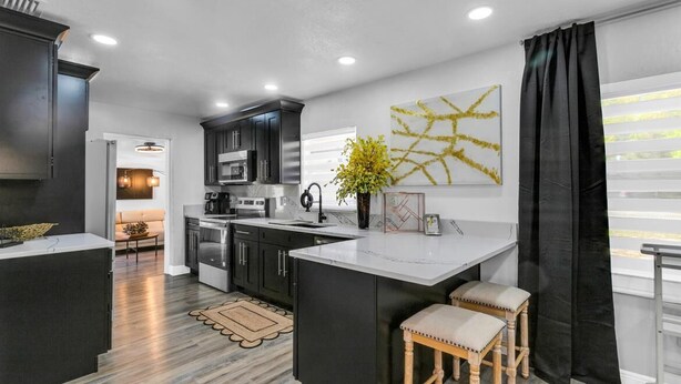 A modern kitchen with dark cabinetry, a central island, and a dining area with stools. - Backyard Zen  Retreat with Modern Vibe (Tampa)