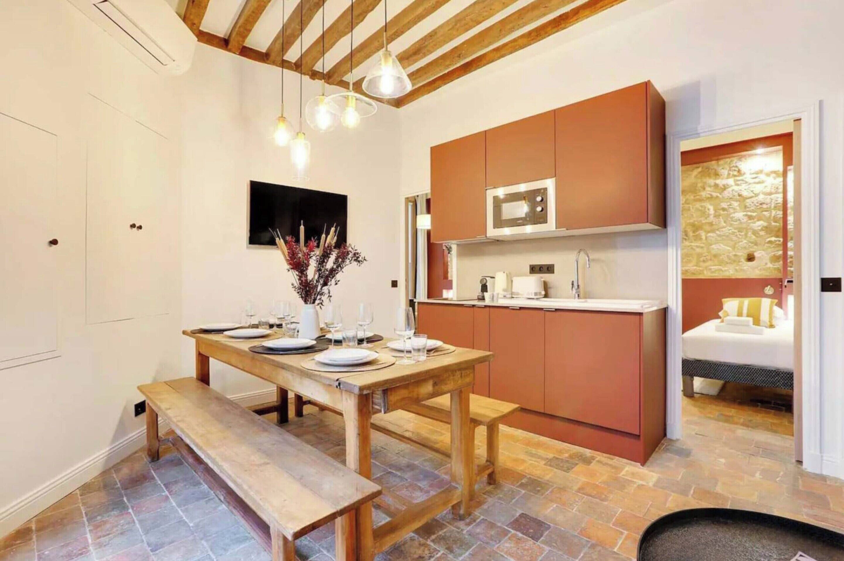 A modern kitchen with wooden cabinets, a built-in microwave, and a dining area with a wooden table and benches.