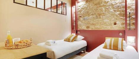 A hotel room with two beds, a stone wall, a wooden desk with breakfast items, and a mirror above the bed.
