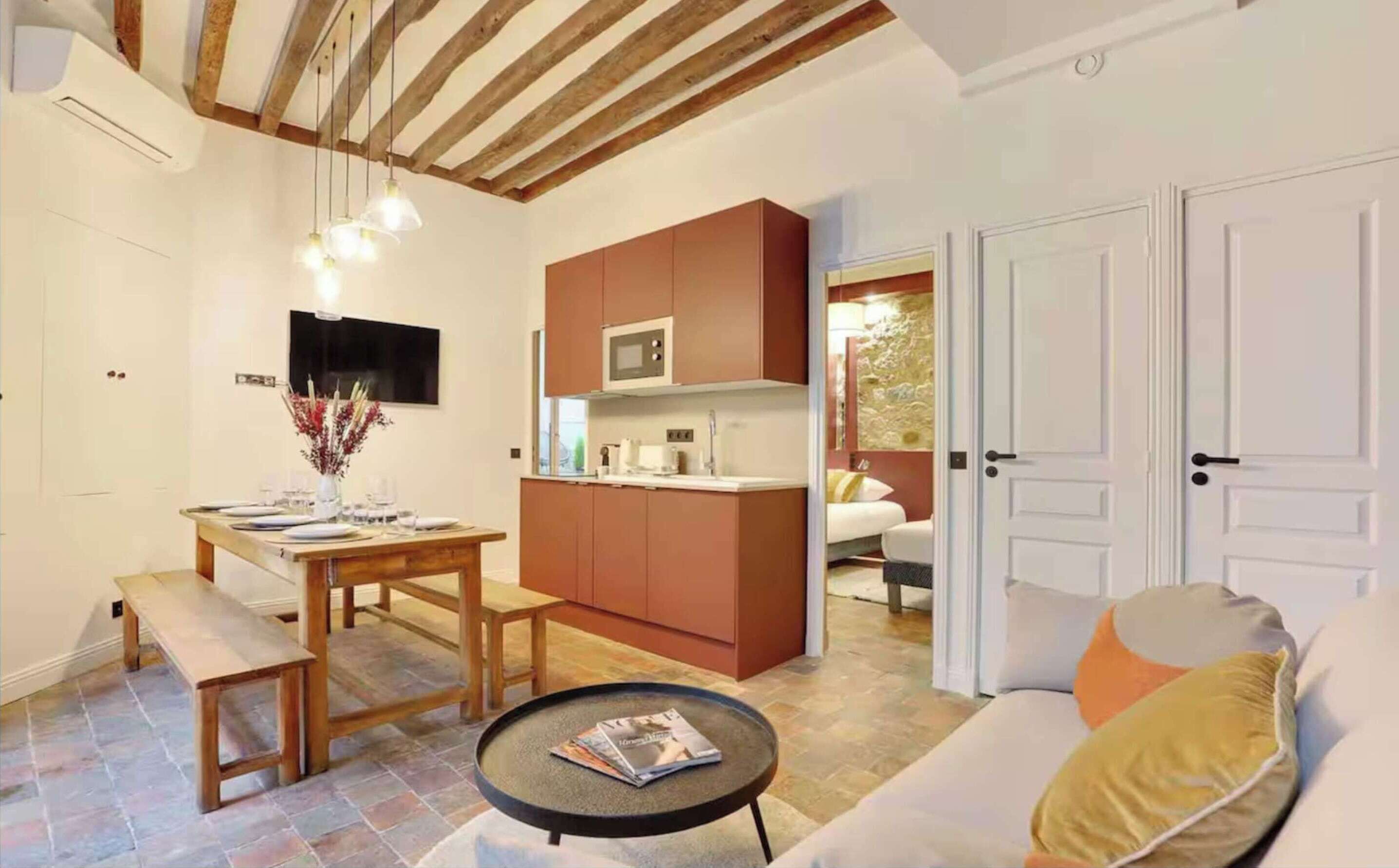 A compact living space with a dining area, kitchenette, and a sofa with cushions.