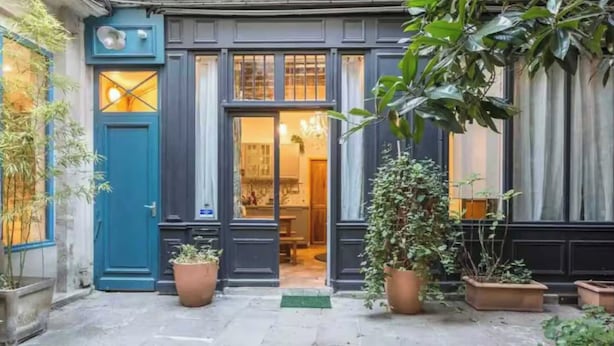 Un edificio con puerta y ventanas azul oscuro, plantas en macetas y un interior visible con comedor.