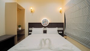 Een hotelkamer met een net opgemaakt bed, een nachtkastje met een lamp, een wandspiegel en een decoratief wandpaneel.