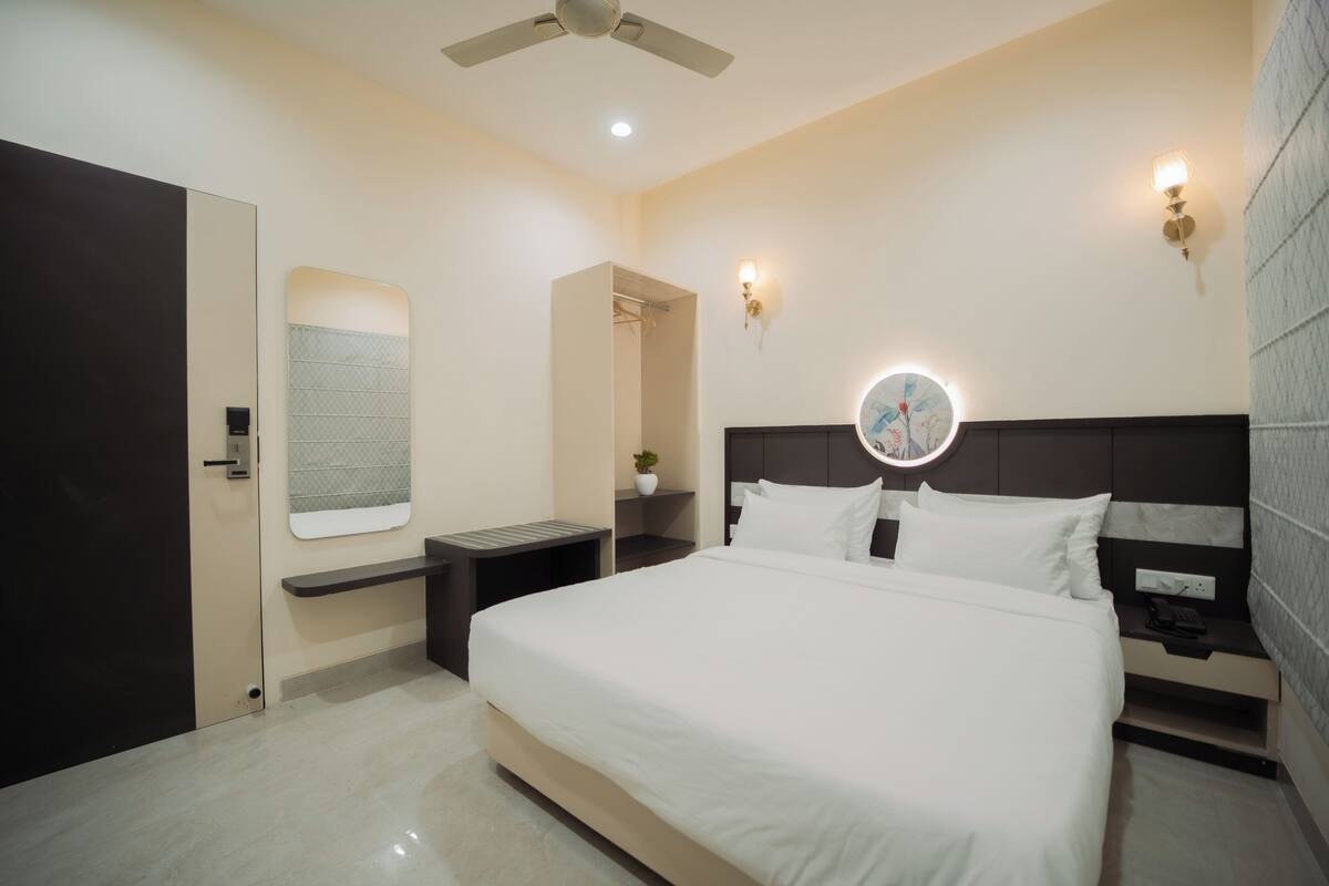 A modern hotel room with a large bed, bedside tables, a ceiling fan, and a round mirror above the bed.