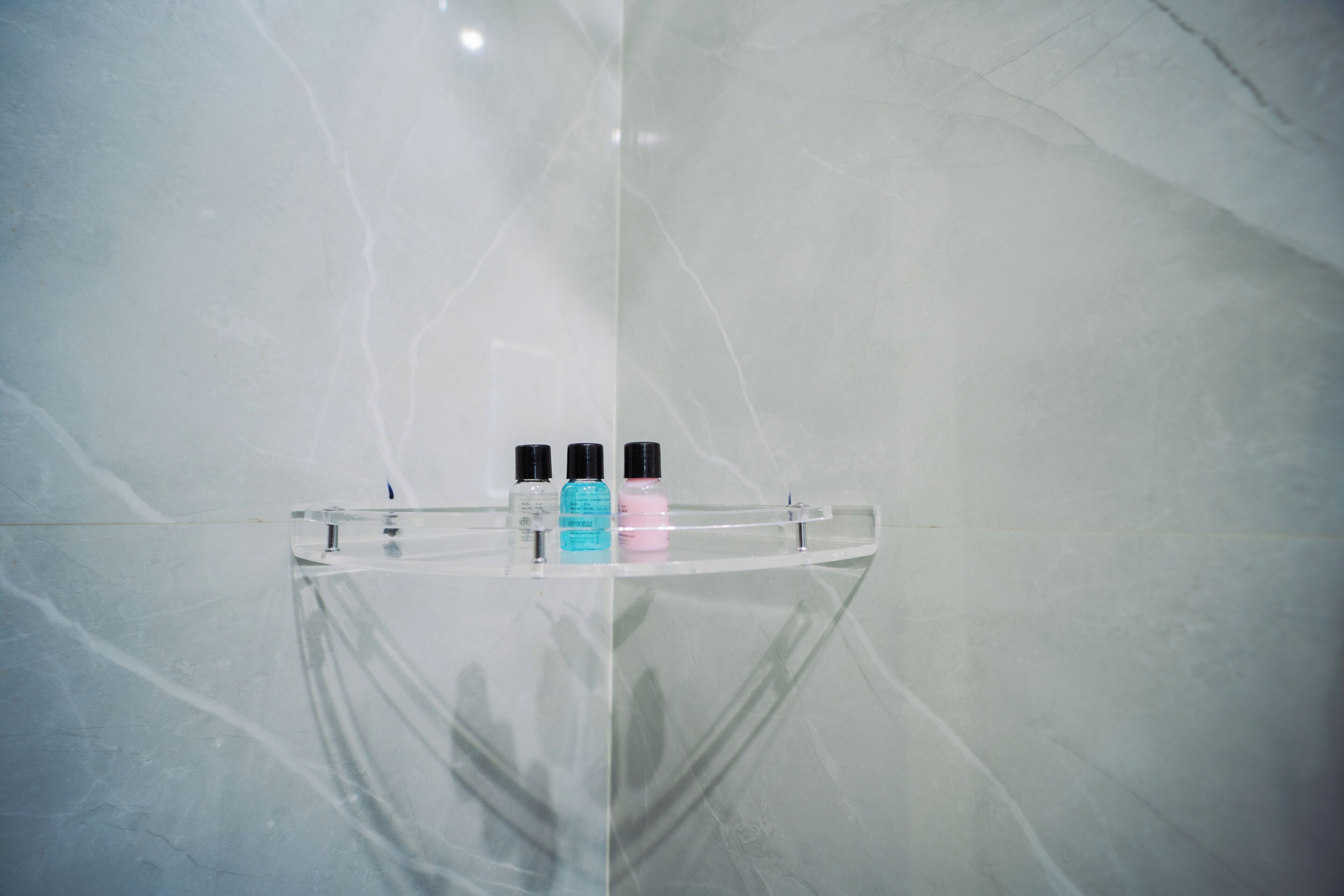 A bathroom with a marble wall and a glass shelf holding three bottles.