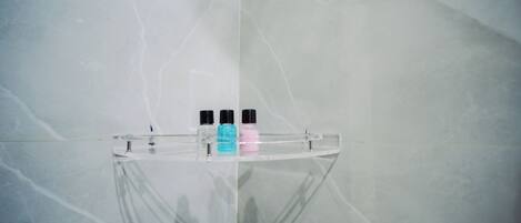 A bathroom with a marble wall and a glass shelf holding three bottles.