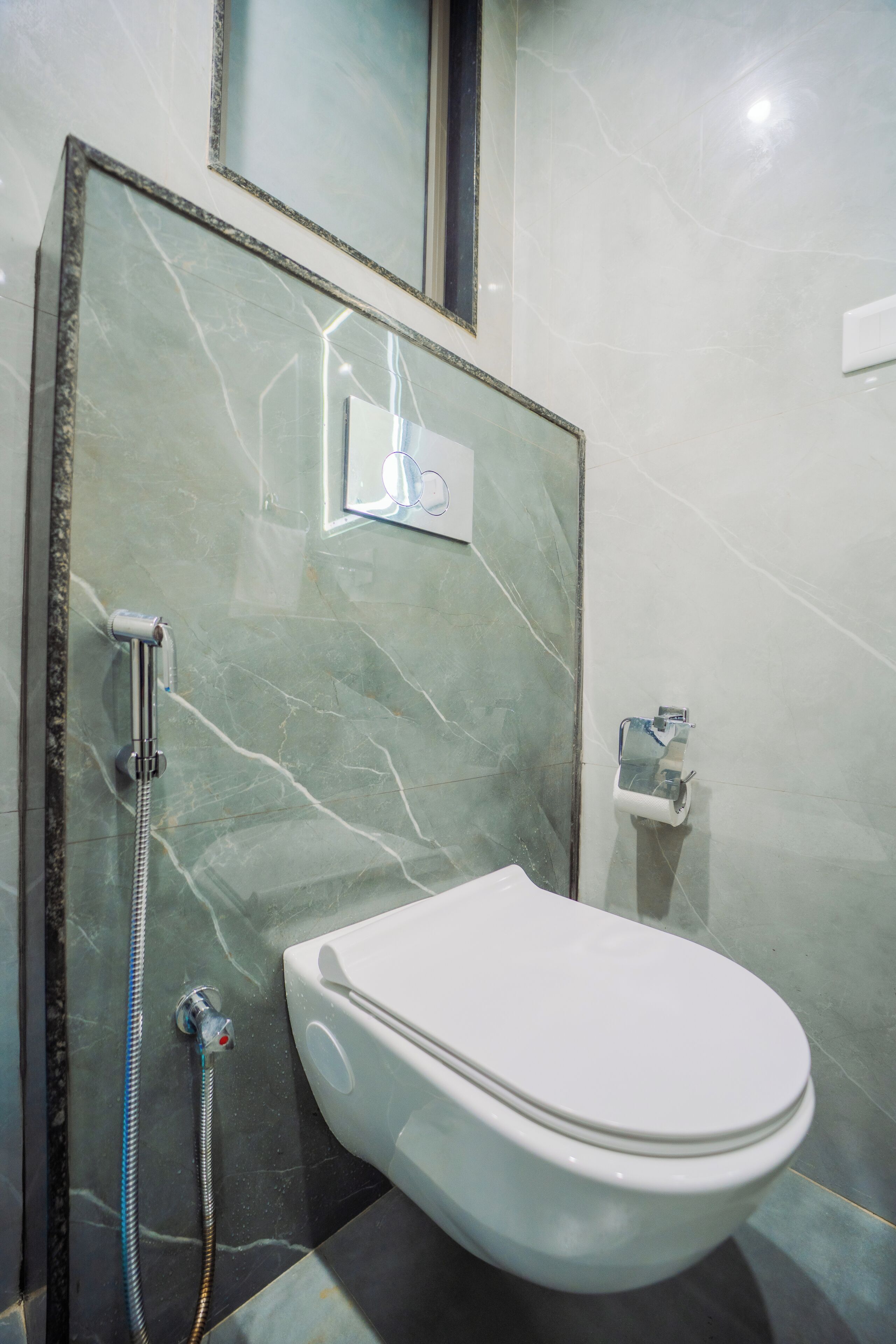 A bathroom with a white toilet, a shower with a handheld hose, and a marble wall.