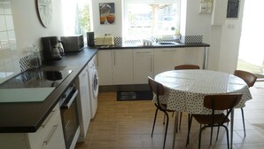 A compact kitchen with a sink, stove, and a dining area with a table and chairs. - The beach at the end of the street (Treffiagat)