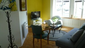 A living room with a television, a sofa, a chair, and a small table. - The beach at the end of the street (Treffiagat)