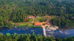 An aerial view of a rural property with a large building, a pond, and dense surrounding forest. - Ekkodlu Homestay (Karkala)